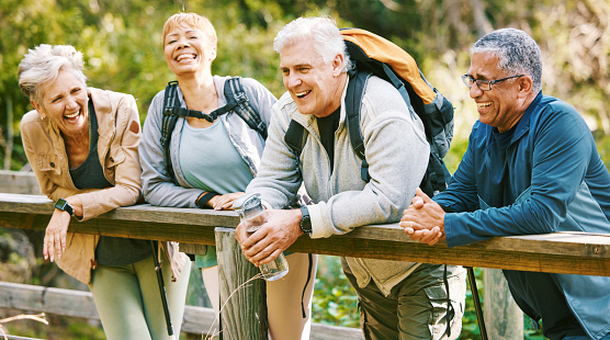 Elderly, people hiking and happy in park with fitness outdoor, relax on bridge while trekking in nature together. Health, wellness and hiker group, sport and active lifestyle motivation with cardio.