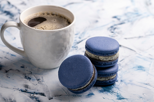 Three blue macaroons and a white cup on a light background close-up
