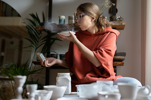 Woman potter using sandpaper, polishing pottery, sanding ceramics while working in cozy studio