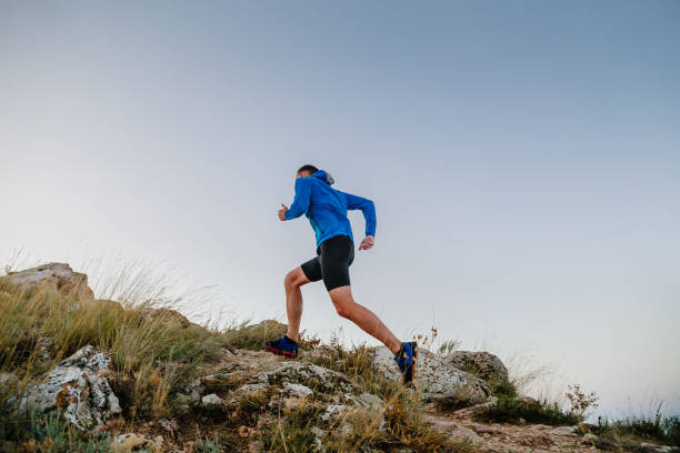 corridore maschile che corre in salita in sfondo blu del cielo - cross country running track and field sports event running foto e immagini stock