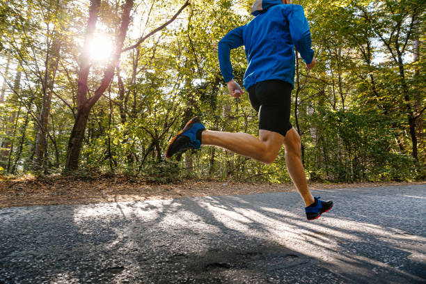 太陽の光の中で公園で道路を走る男性ランナー - scoring run ストックフォトと画像