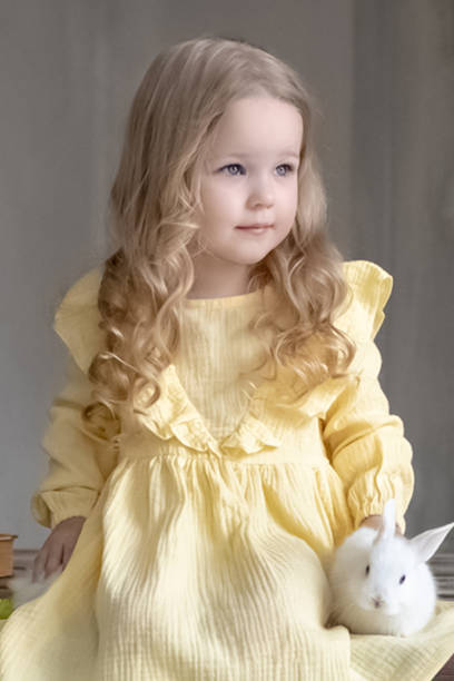 une petite fille souriante en robe jaune est assise avec des lapins sur une table en bois avec des fleurs. un bébé et un lapin. le concept de pâques. - child easter flower little girls photos et images de collection