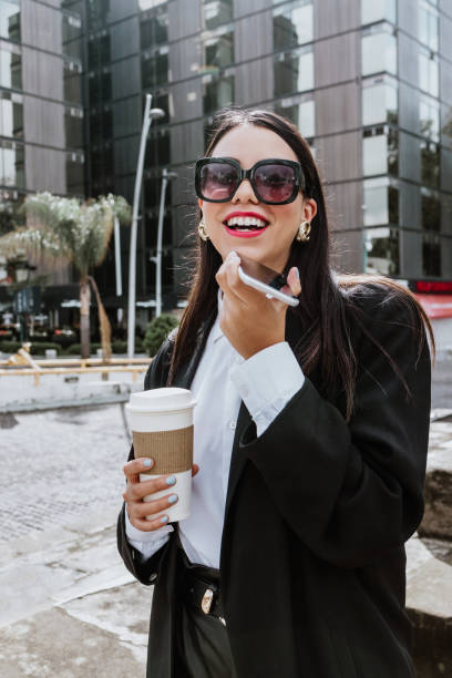 istock Young hispanic businesswoman in coat with coffee cup and talking on mobile phone  while intently looking away on city street in Mexico Latin America 1470679820