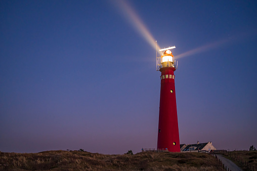 A lighthouse on a tropical island on the ocean with a beam of light in the night sky with stars