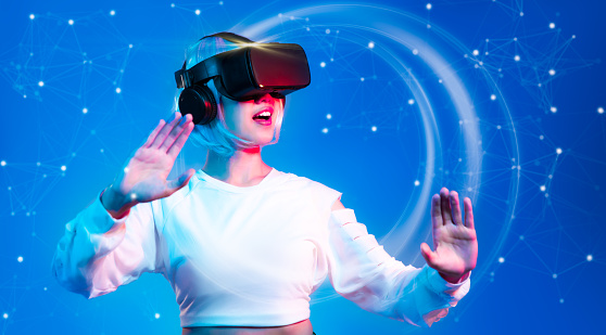 Metaverse technology. Asian woman wearing vr goggles headset watching, playing connecting virtual game blue background.