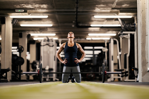 A motivated bodybuilder is kneeling in a gym and preparing to lift heavy barbell.