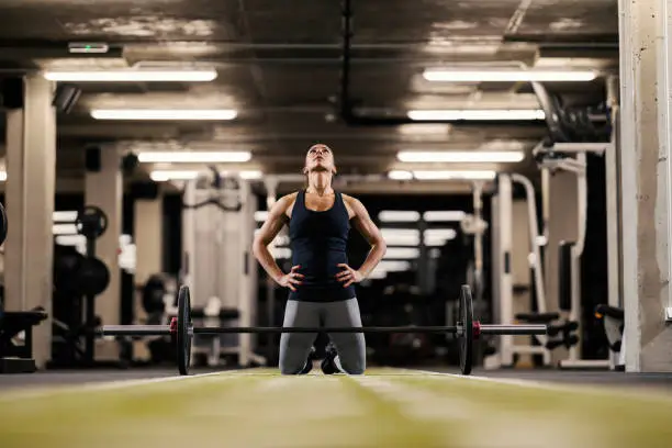 Photo of A female bodybuilder is motivating herself and preparing to lift barbell while kneeling in a gym.