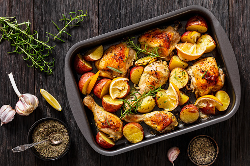 Lemon Garlic Chicken with roasted potatoes, spices and herbs on Sheet-Pan on dark wood table with ngredients, horizontal view from above, flat lay
