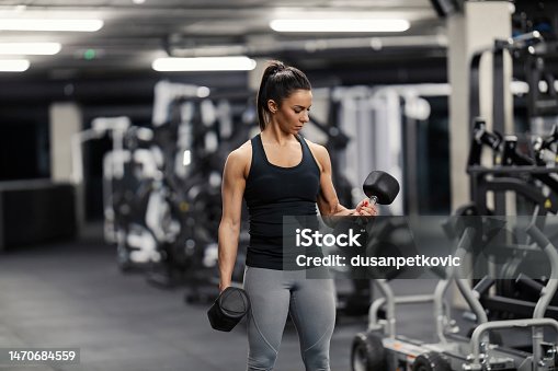istock A fit sportswoman in shape is doing exercises for biceps with dumbbells in a gym. 1470684559