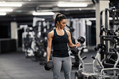 A fit sportswoman in shape is doing exercises for biceps with dumbbells in a gym.