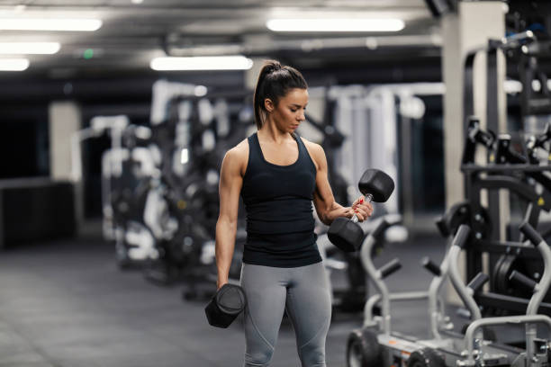 A fit sportswoman in shape is doing exercises for biceps with dumbbells in a gym. stock photo