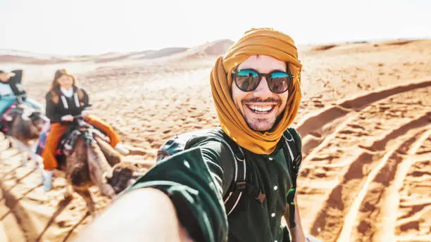 Photo of Happy tourist having fun enjoying group camel ride tour in the desert - Travel, life style, vacation activities and adventure concept