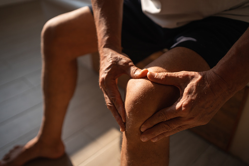 Unrecozgniable senior man is using a hand to massage his knee, in an effort to alleviate pain or discomfort.
