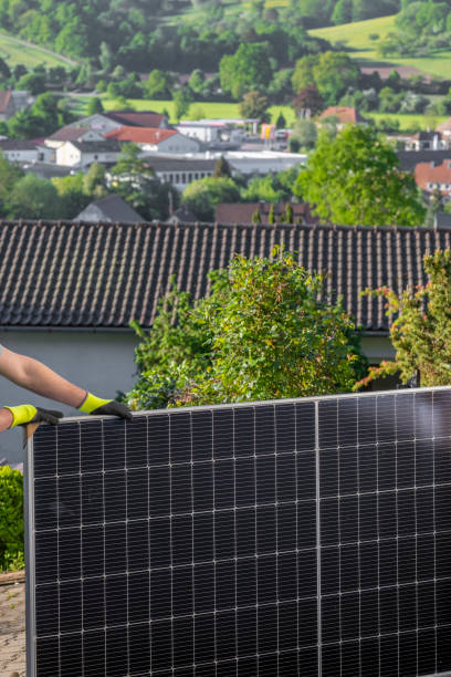 istock renewable energy.Installation of energy light modules in a private house.Solar panel in the hands of a worker on city houses background.Fitting solar panels. 1470689267