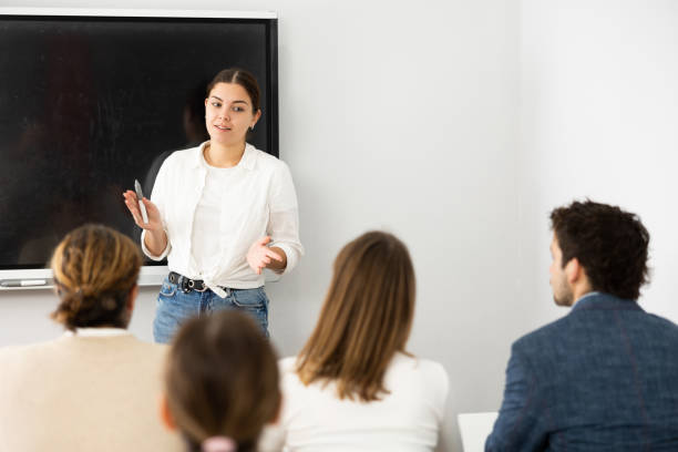 istock Positive female trainer standing near interactive board and conducting advanced training courses to office employees sitting at desks in classroom 1470691106