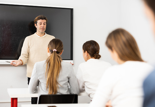 Male trainer near interactive board conducting advanced training courses to office employees sitting at desks in auditory