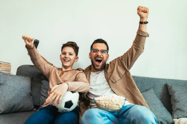 istock Boy watching soccer match with father at home, sitting on sofa 1470691651