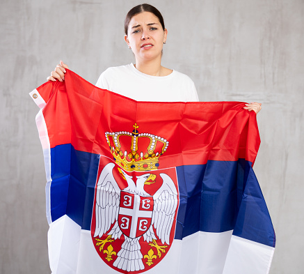 Frustrated girl with  flag of Serbia in her hands.   Isolated on  gray background