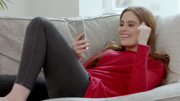 Surprise winner,  young woman with a smartphone lying on a sofa.