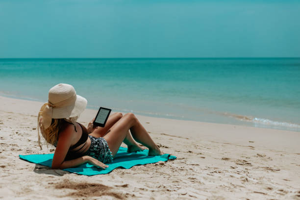 istock Woman with an e-reader on vacation at the beach reading a book 1470692672