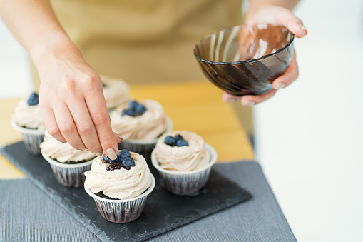 Women's hands of a confectioner, decorating cupcakes with blueberries and chocolate. Close-up, space for text
