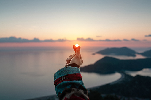 Travel in her heart. Woman makes heart from fingers sun at sunset