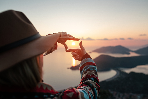 Tourist woman makes finger frame on sea and islands at sunset