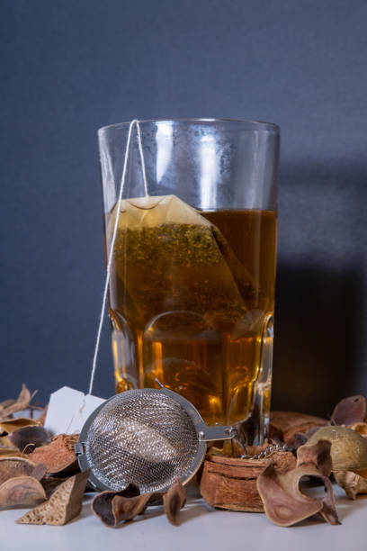 istock Glass cup with hot infusion and the tea bag inside with an infuser next to it surrounded by dried flowers on a black background. 1470703864