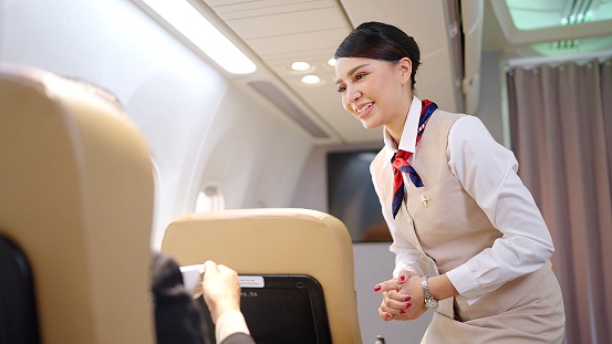 Friendly Asian female flight attendant serving food drink and talking to passengers on airplane. Airline service