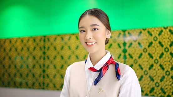 Asian female airline worker stewardess in aviation air hostess uniform looking at camera and smiling