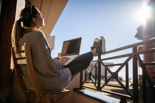 istock Young woman using laptop on balcony at morning 1470708973