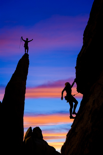 A team of climber is silhouetted against the evening sky as they ascend a steep rock face in Joshua Tree National Park, California.