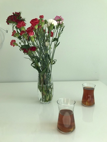 Red carnations in a vase, on the table home decor and two cups of turkish tea