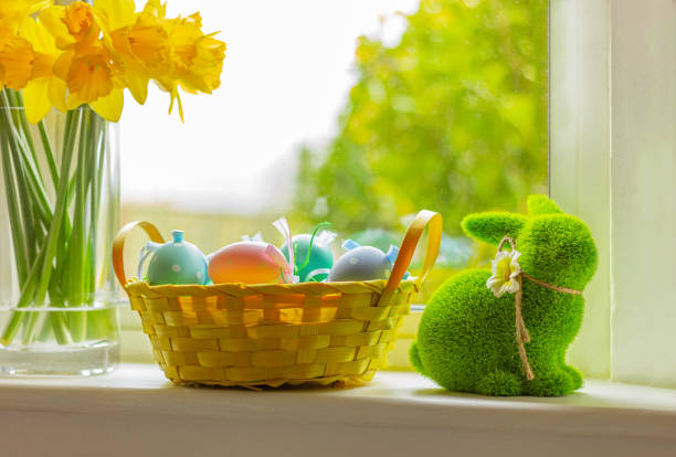istock rabbit and basket with colorful eggs on window sill with flowers. Easter symbol, decor, green grass bunny figure 1470711016