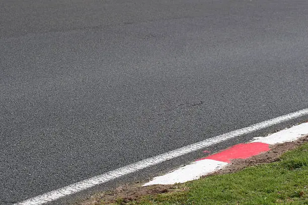 Red and white painted kerbs edge smooth tarmac at a motorsport venue.
