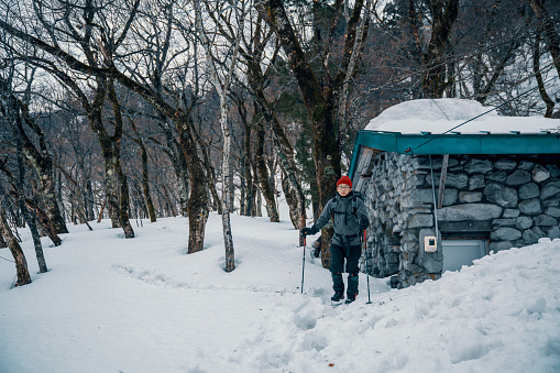 Mid adult male walking through a snowy forest away from a vacation rental in the mountains of rural Japan