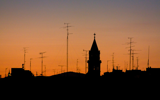TV antennas, chimneys and a church bell tower silhouetted,  beautiful sunset background. Madrid, Spain.