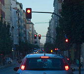 Driving at dusk, stop sign, red traffic lights, rear view of car waiting.
