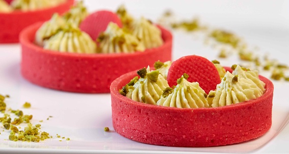 Sweet dessert: Tarts, Tartlets. Bright red baskets of shortbread dough and a delicate green pistachio filling. Close-up on a white plate