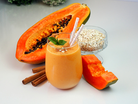 Half papaya fruit, oatmeal in a glass bowl, light orange smoothie with green leaves and straws. Diet drink.