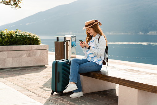 Portrait of a beautiful young woman on a vacation taking a break on the street and using smartphone