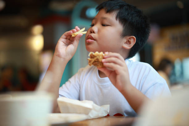 Little Asian boy aged 11 enjoying unhealthy food. He is having burgers and fried in restaurant.