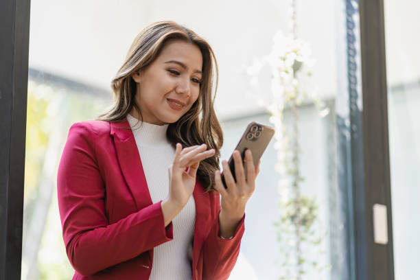 istock Asian female worker sitting in remote office holding smartphone using business applications or mobile work tools. Female freelancer checking email on mobile phone 1470722018