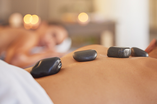 Stone, man or woman at a spa for a massage, relaxing self care or luxury physical therapy healing for back pain. Hot stone massage, zoom or customer on a bed for healthy natural holistic treatment