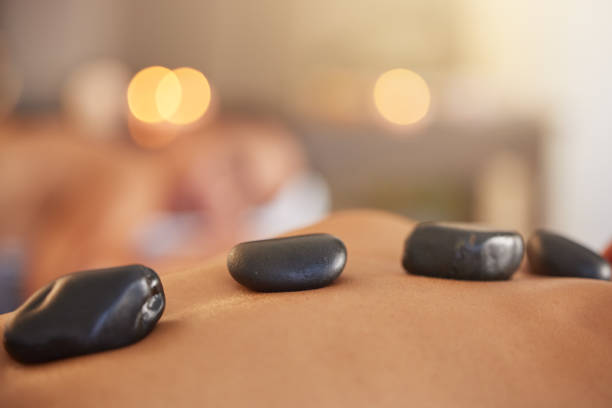 stone, homme ou femme dans un spa pour un massage, des soins personnels relaxants ou une thérapie physique de luxe pour la guérison des maux de dos. massage aux pierres chaudes, zoom ou client sur un lit pour un traitement holistique naturel sain - lastone therapy spa treatment massaging massage therapist photos et images de collection