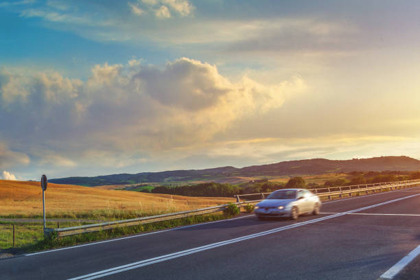 This photo captures the beauty of a highway in Tuscany at sunset. The sun's warm orange and pink hues illuminate the fields of yellow wheat along the road, creating a serene and peaceful atmosphere. A motion-blurred car rushes down the highway, adding a sense of movement and speed to the scene. The colors of the sunset and the contrast of the yellow wheat against the blue sky create a harmonious and calming effect. This photo perfectly captures the essence of Tuscany, with its gentle rolling hills and iconic countryside. It evokes a sense of freedom and adventure, inviting the viewer to hit the open road and explore the beauty of the world around us.