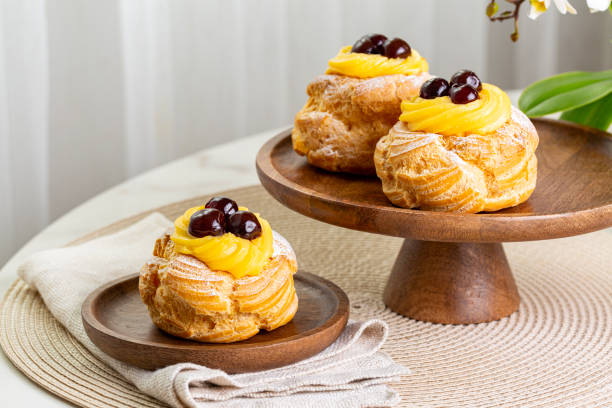 Table with Italian pastry - zeppole di San Giuseppe - baked puffs made from choux pastry, filled and decorated with custard cream and cherry.  Saint Joseph's Day. stock photo