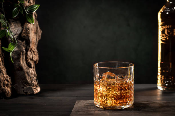 glass of whisky with ice and bottle on wooden table on dark background with copy space. - brandy bottle alcohol studio shot imagens e fotografias de stock