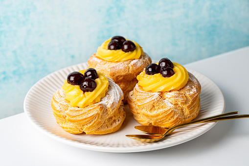 Italian pastry - zeppole di San Giuseppe, zeppola - baked puffs made from choux pastry, filled and decorated with custard cream and cherry.  Saint Joseph's Day. White and blue background.