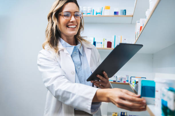 Happy pharmacist getting prescription medication from a shelf in a chemist. Happy pharmacist getting medication from a shelf in a chemist. Female healthcare worker filling prescriptions using a tablet. Woman working in a pharmacy. pharmacist stock pictures, royalty-free photos & images